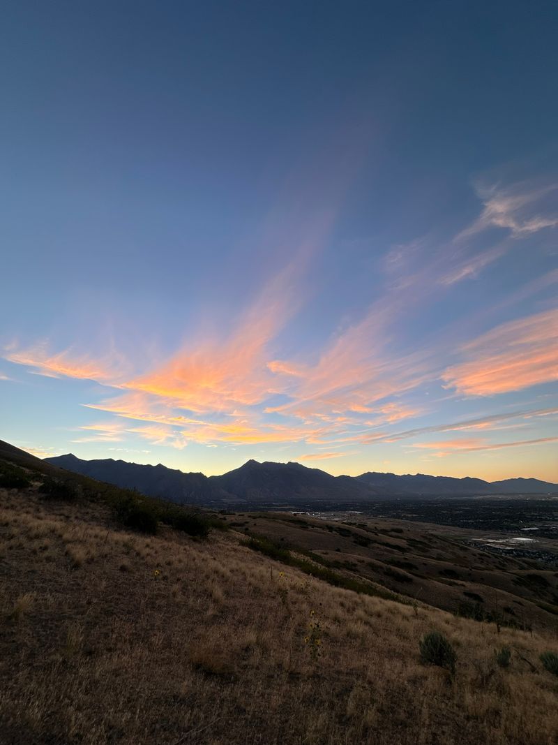 Pink and gold streaks of cloud over a mountain ridge, a dry grass hillside in front.