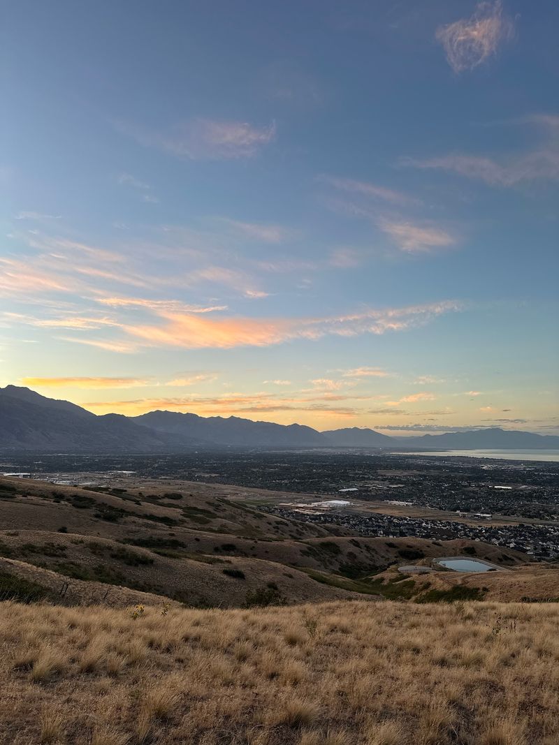 Thin peach clouds in a blue sky over a dry grass hillside and a wide valley.